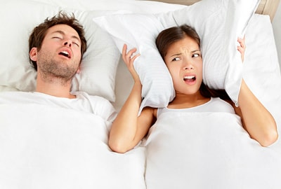 A men snoring next to a woman holding a pillow
